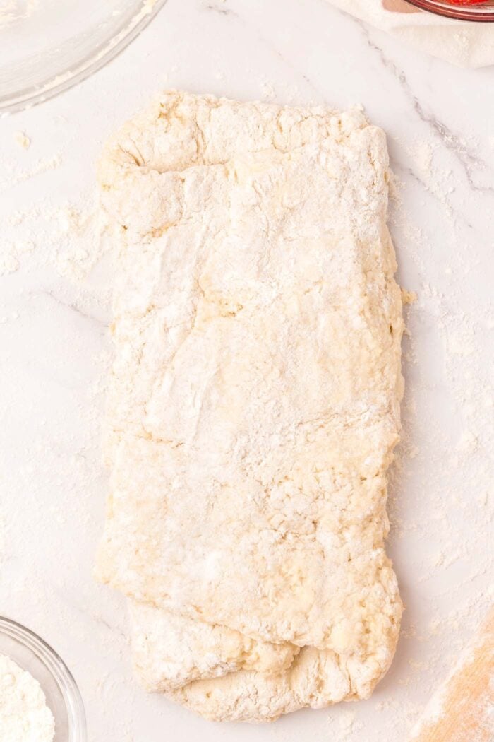 A rectangle of biscuit dough on a floured marble surface.