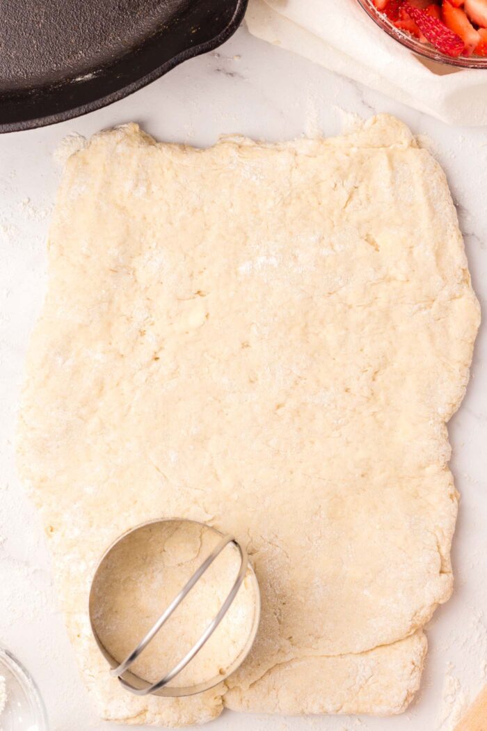 A biscuit cutting sitting on a rectangle of biscuit dough.