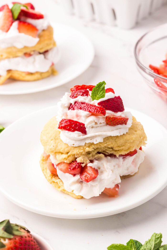Strawberry shortcakes topped with a small piece of mint on small round plates.