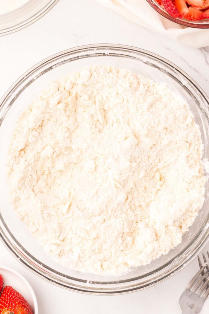 A bowl of flour with cold butter mixed into it making it a crumbly.