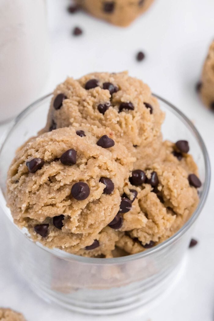 Close up of scoops of edible chocolate chip cookie dough in a glass bowl.