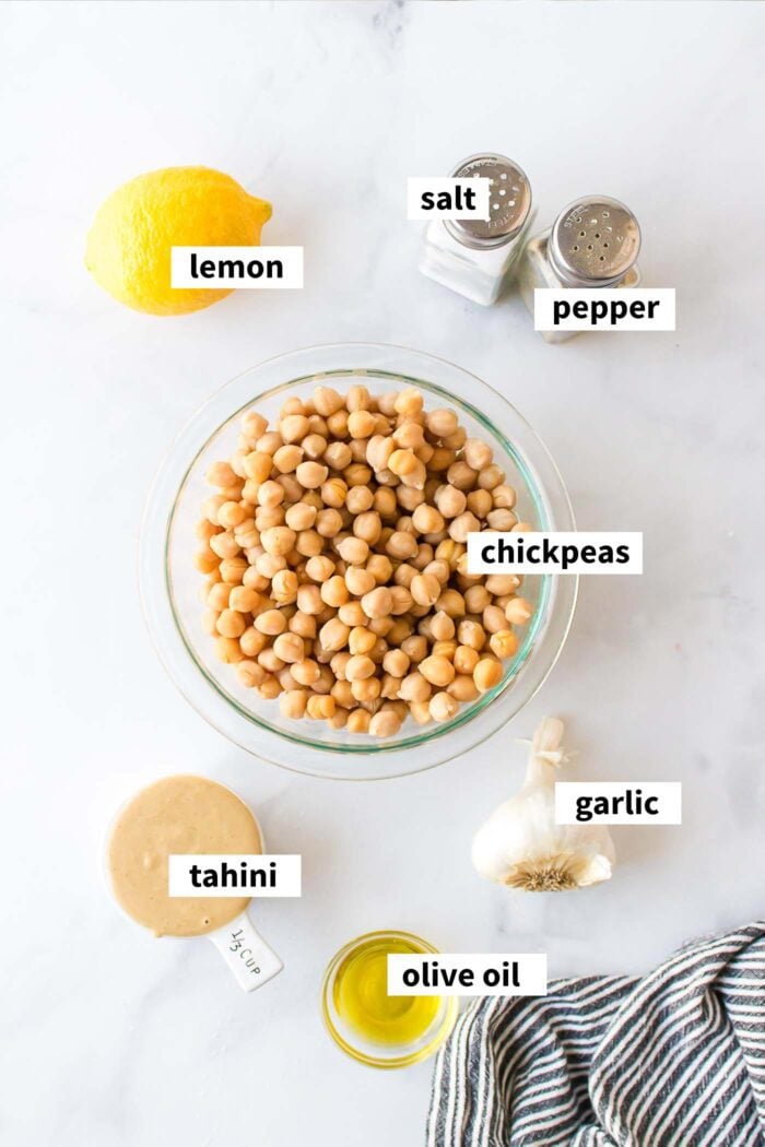 Ingredients needed for making a roasted garlic hummus recipe with tahini, lemon, chickpeas and olive oil.