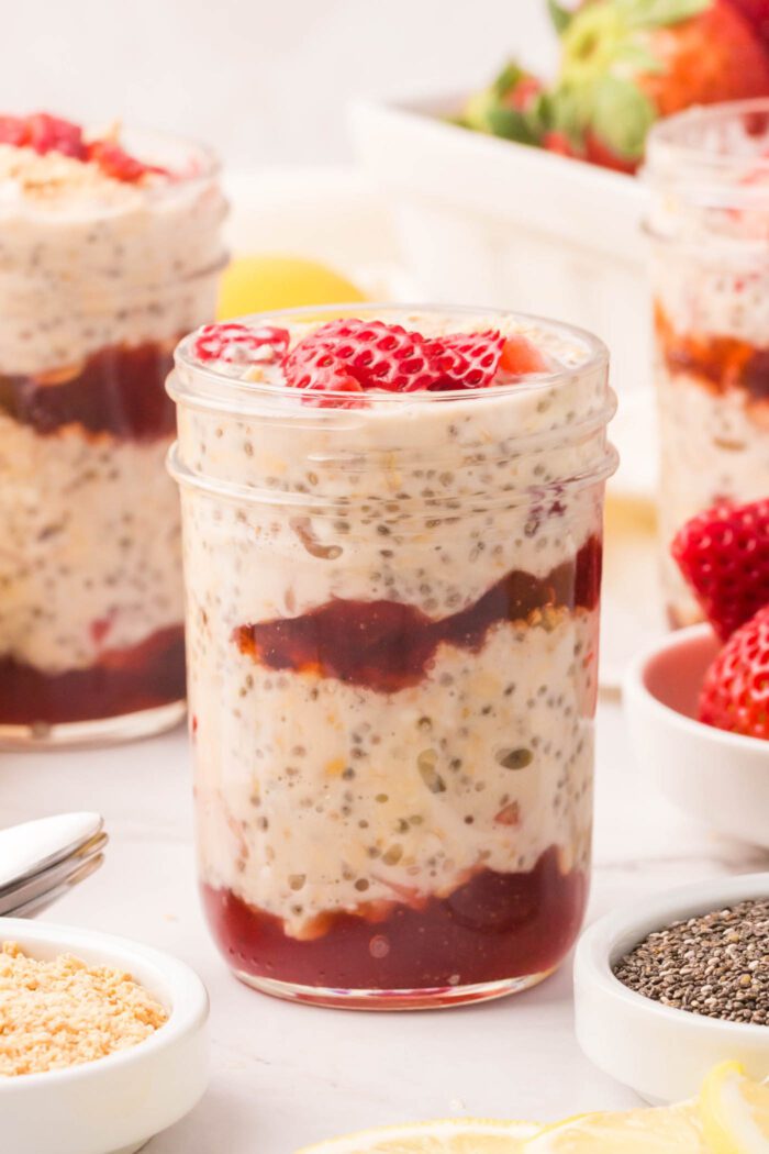 3 jars of overnight oats layered with strawberry jam and topped with fresh strawberries.