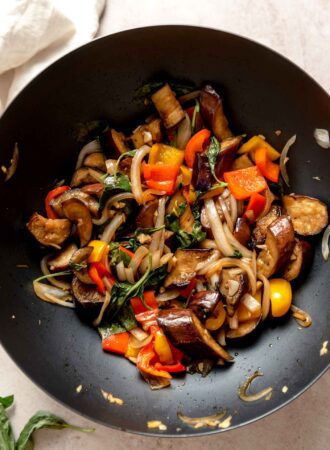 Overhead view into a wok of stir fried Thai basil eggplant with peppers and onions.