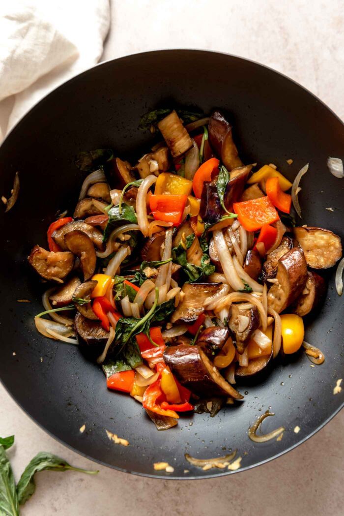 Overhead view into a wok of stir fried Thai basil eggplant with peppers and onions.