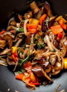 Stir fried Thai basil eggplant cooking in a wok with bell peppers and onions.