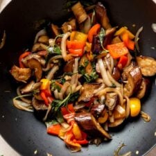 Stir fried Thai basil eggplant cooking in a wok with bell peppers and onions.