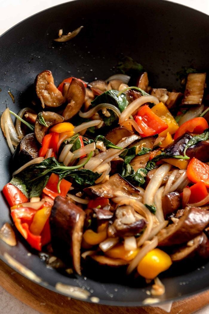 Stir fried eggplant, peppers, onions and Thai basil in sauce cooking in a large wok.