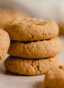 A stack of 3 small peanut butter cookies with another cookie leaning against the stack. The cookies have a crisscross pattern on top.