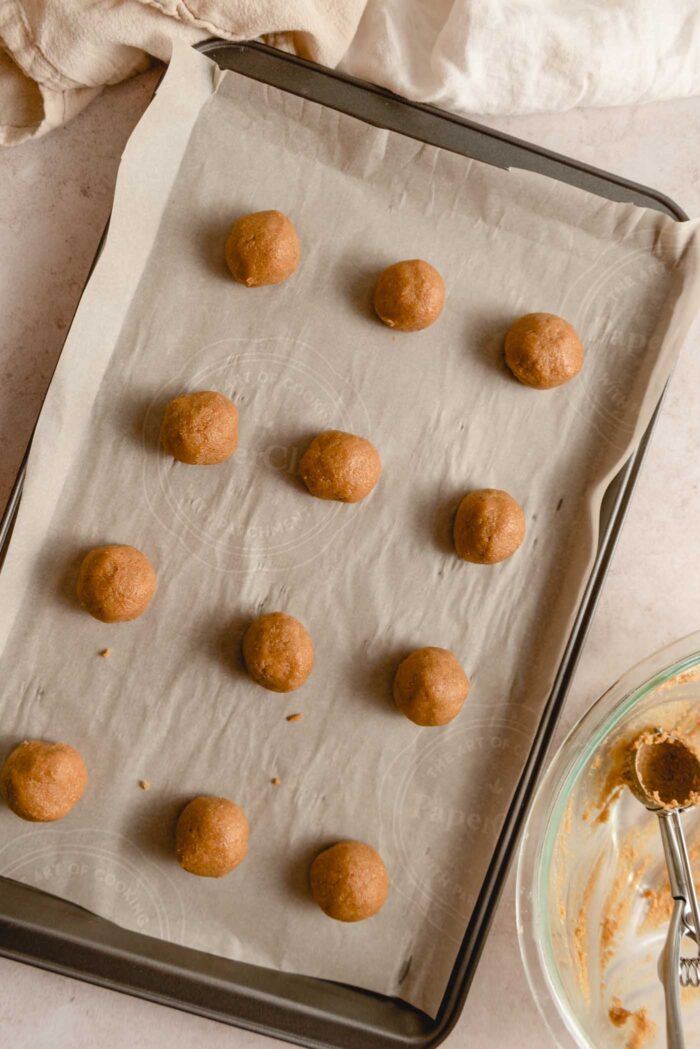 12 balls of of peanut butter cookie dough on a baking sheet lined with parchment paper.
