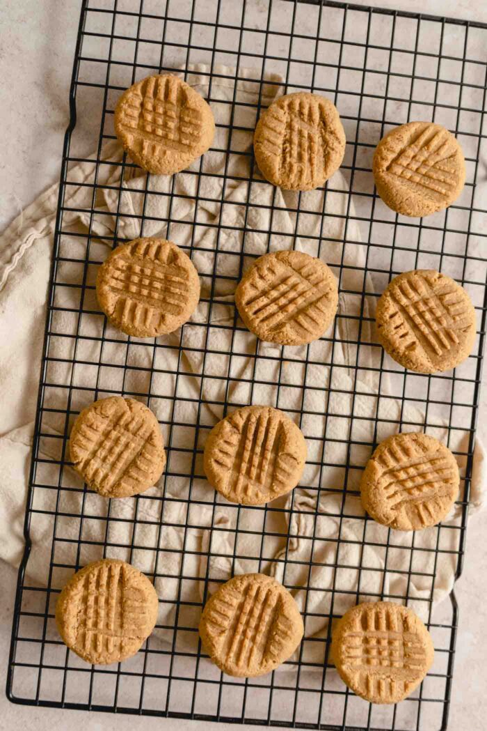 12 baked peanut butter cookies with a crisscross pattern on top cooling on a baking rack.
