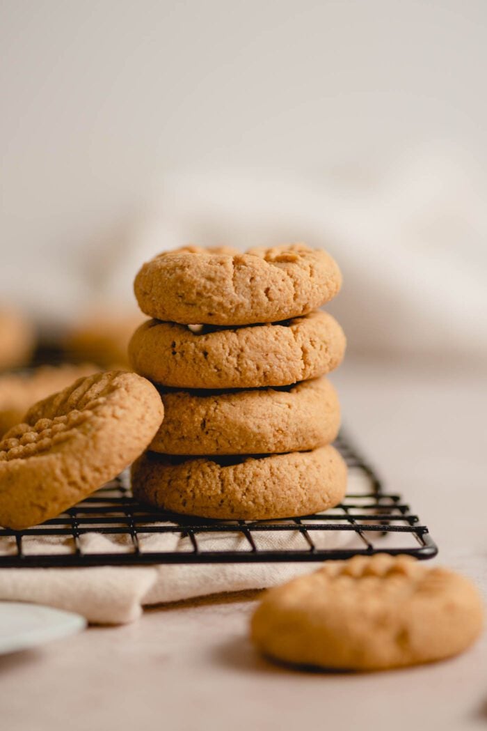 A stack of 4 peanut butter cookies sitting on the edge of a baking cooling rack.