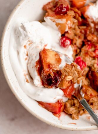 Close up of a bowl of cranberry apple crisp with whipped cream on top and a spoon in the bowl.