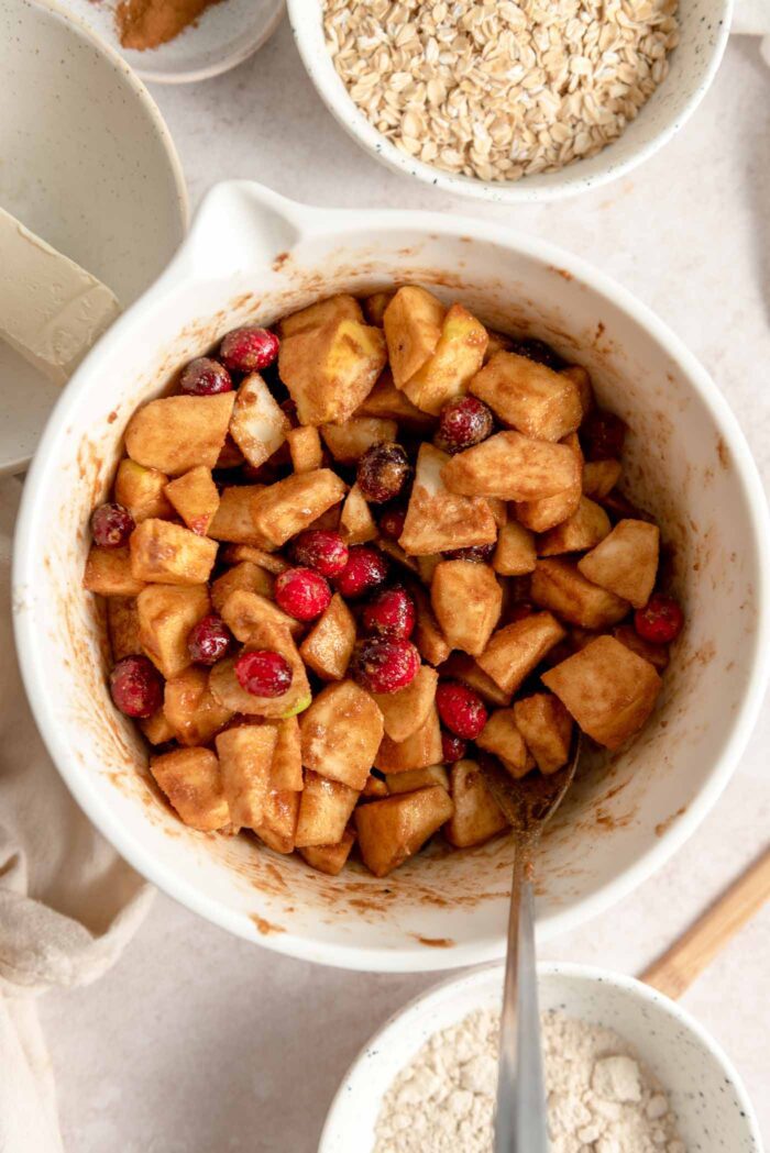 Chopped apples and fresh cranberries coated in a brown sugar mixture in a mixing bowl.