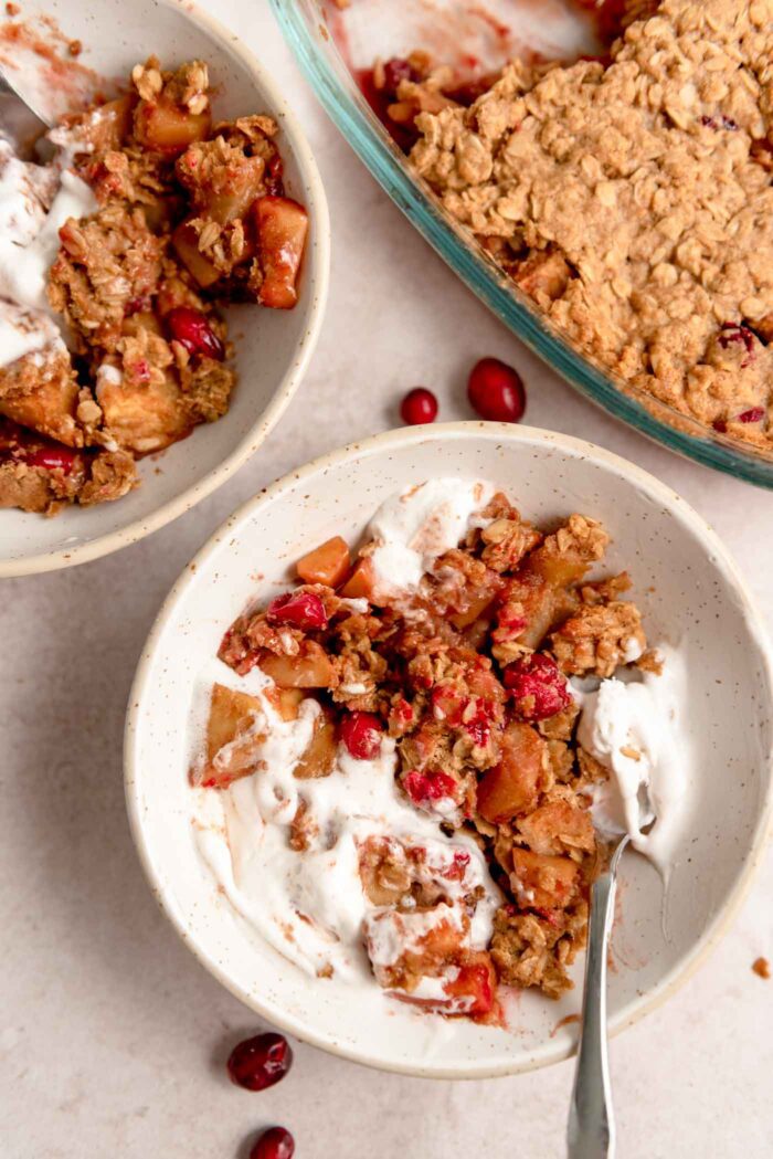 A bowl of cranberry apple crisp with whipped cream and a spoon in it.
