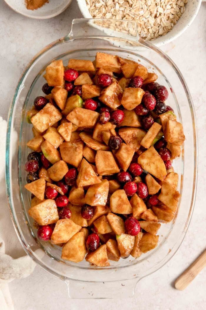 An apple cranberry crisp filling in a glass oval baking dish.