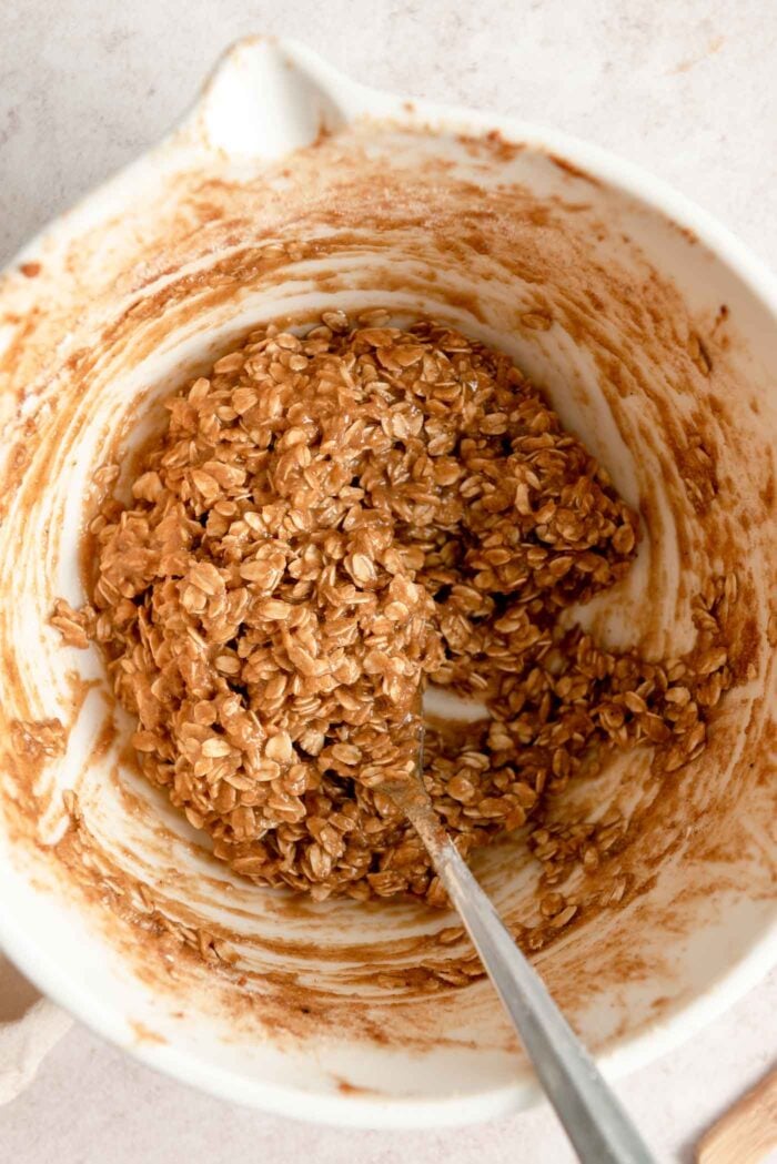 Oatmeal crumble topping mixture mixed up in a mixing bowl with a spoon in it.