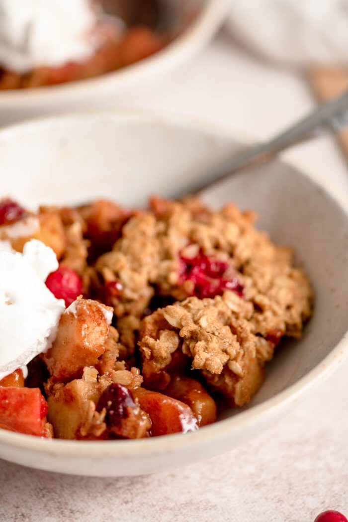 A bowl of cranberry apple crisp topped with whipped cream.