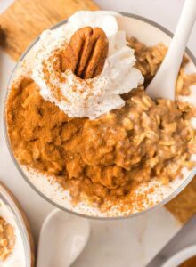 Overhead view of a parfait glass of pumpkin overnight oats topped with whipped cream a pecan and cinnamon.