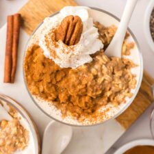 Overhead view of a parfait glass of pumpkin overnight oats topped with whipped cream a pecan and cinnamon.