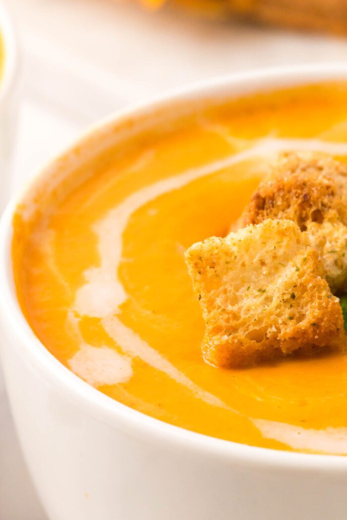 Close up of a bowl of creamy vegan tomato soup drizzled with coconut milk and topped with croutons.