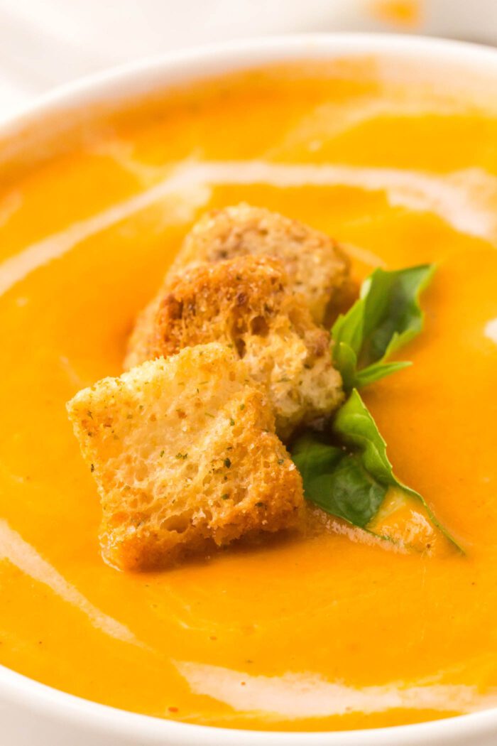 Close up of a bowl of creamy tomato basil soup topped with croutons and fresh basil.