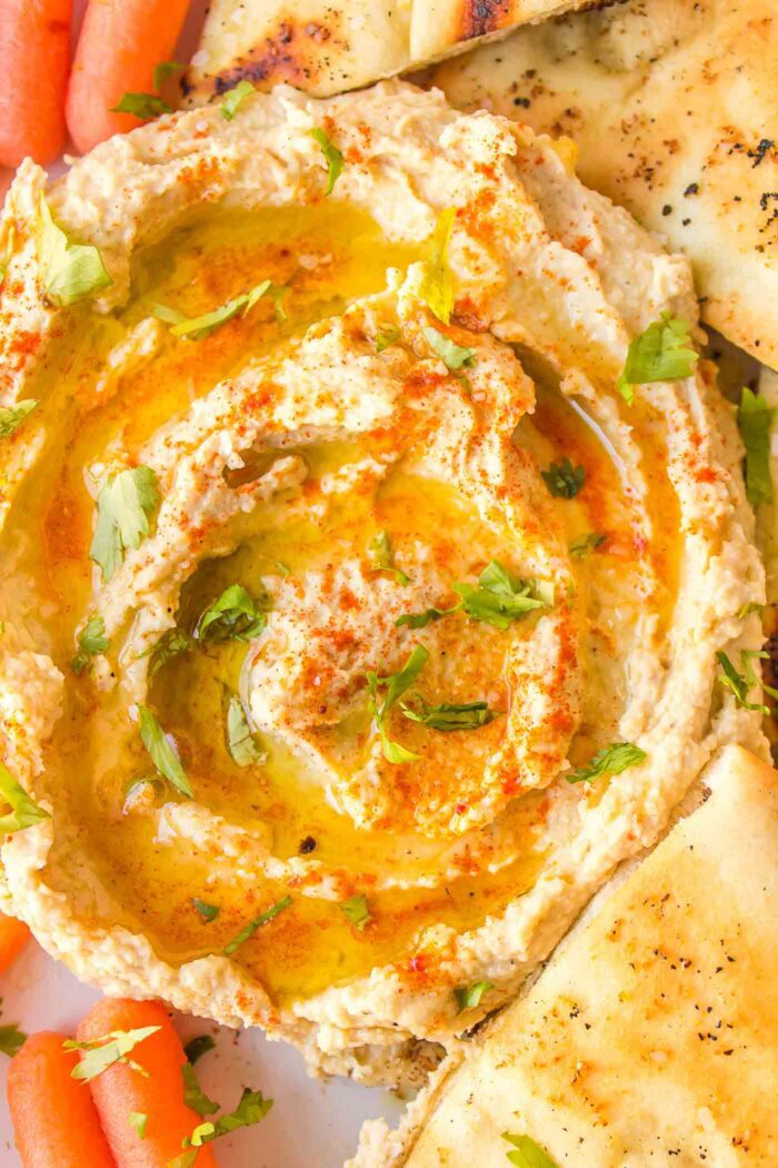 Creamy hummus drizzled with olive oil surrounded by wedges of pita and baby carrot.
