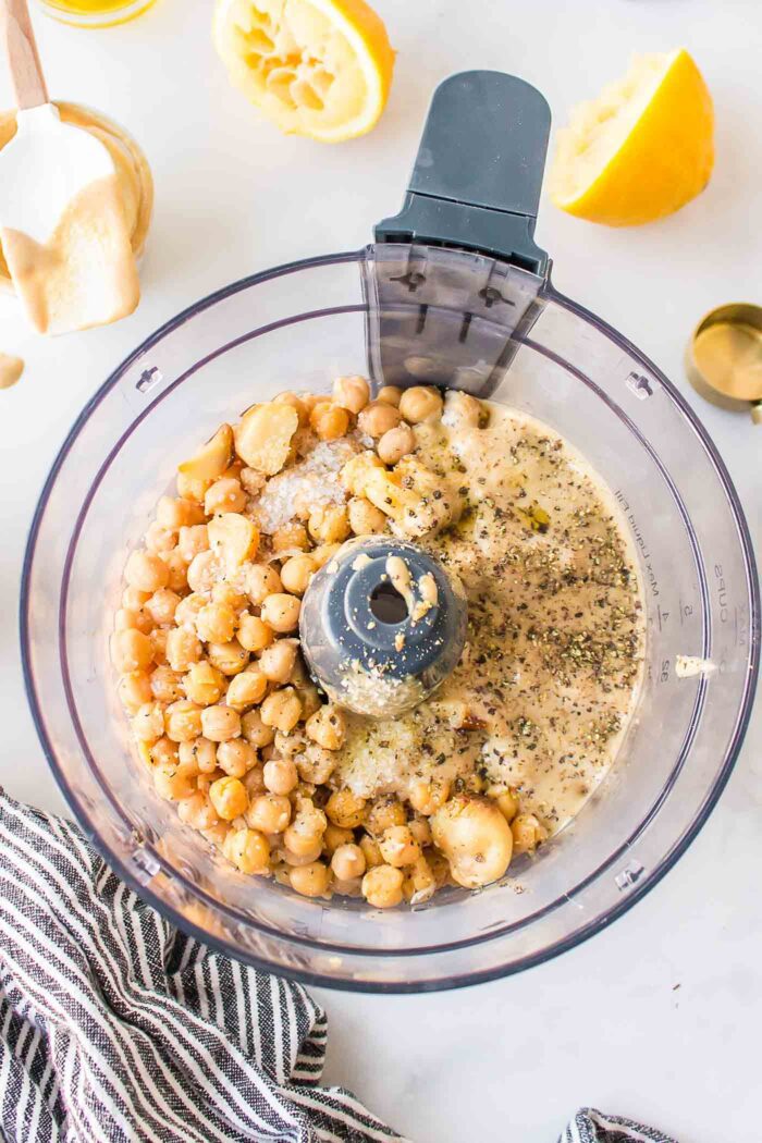Chickpeas, tahini and cloves of roasted garlic in a food processor container.