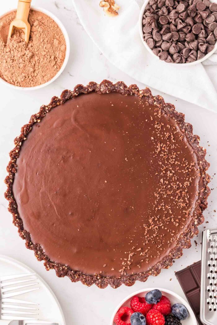 Overhead view of a beautiful dark chocolate ganache tart dusted with cocoa powder in a tart pan.