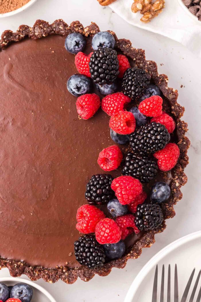 Overhead view of a chocolate ganache tart topped on one half with fresh raspberries, blueberries and blackberries.
