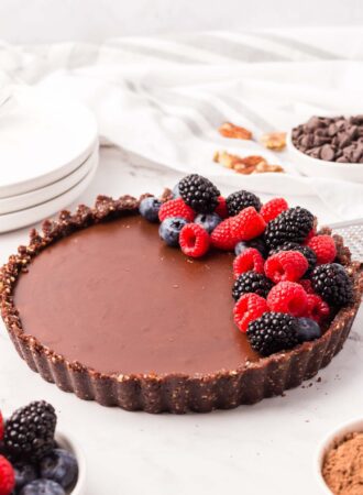 A chocolate ganache tart with a chocolate crust topped with a pile of fresh berries on one side.