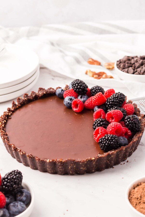 A chocolate ganache tart with a chocolate crust topped with a pile of fresh berries on one side.