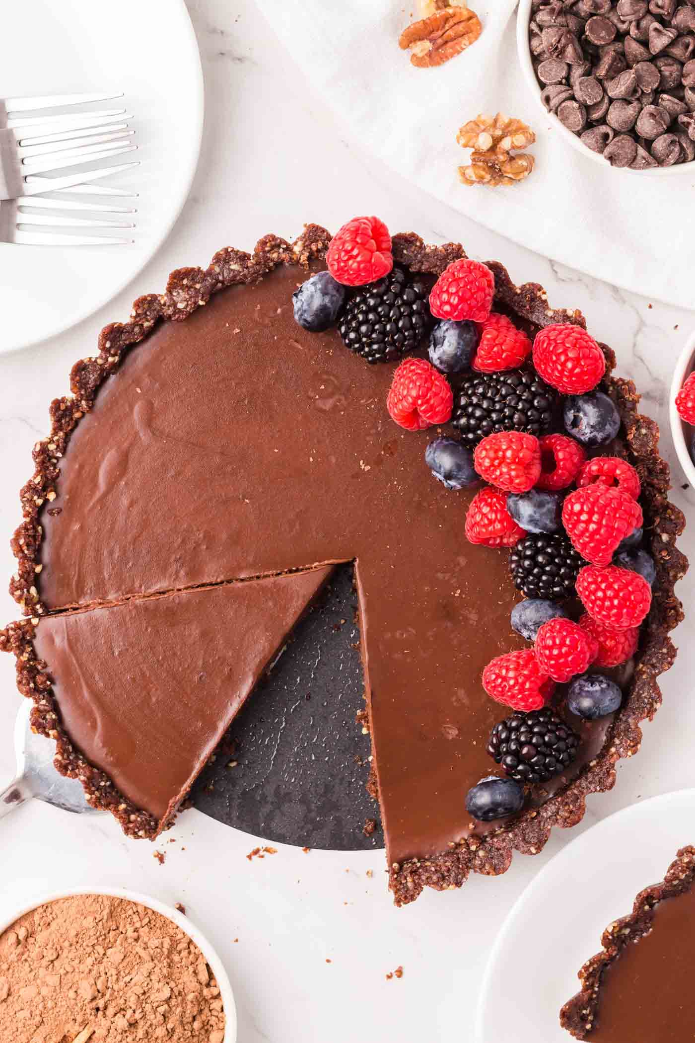 A chocolate ganache tart topped with fresh raspberries and blueberries with a slice out of it.