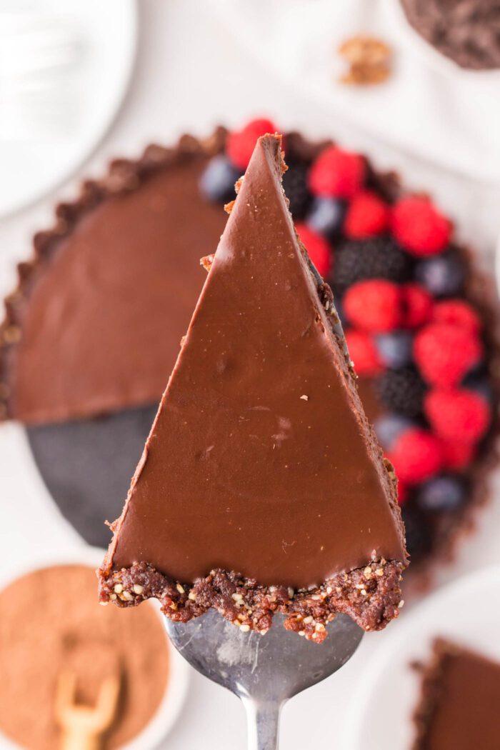 A slice of dark chocolate ganache tart on a spatula held over the whole tart underneath it.