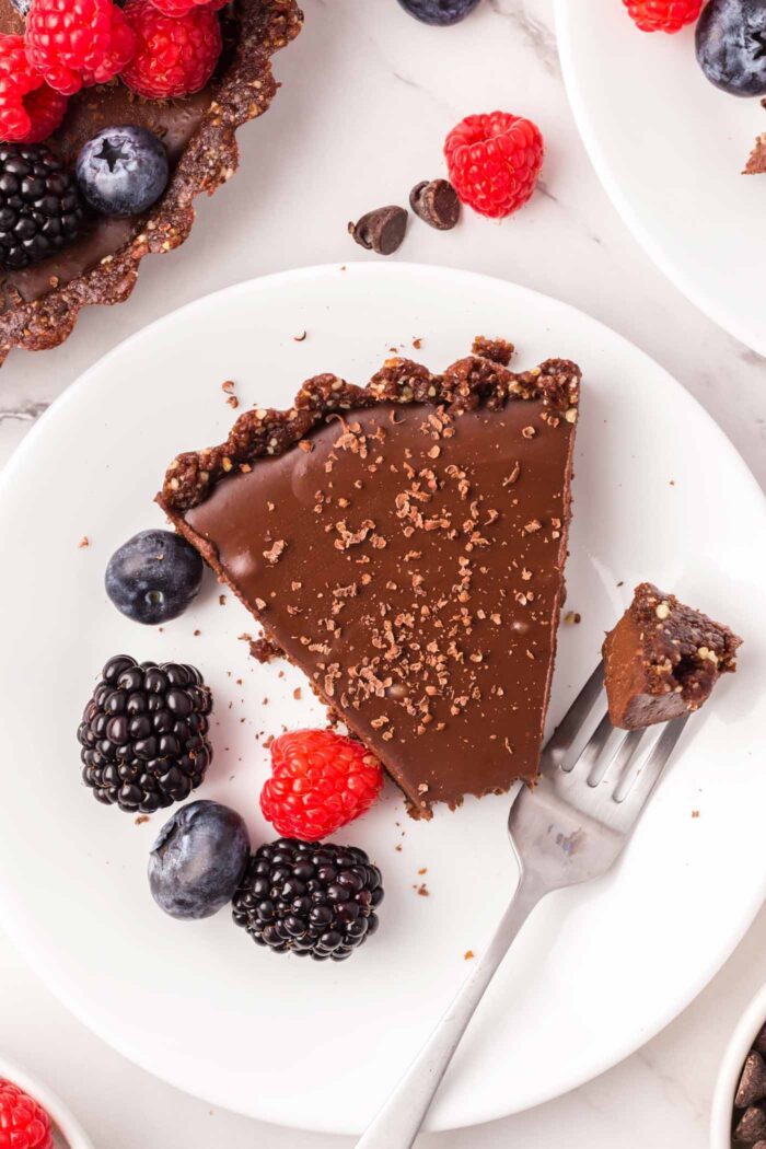A slice of a chocolate tart on a plate with a fork that's taken a piece out of the tart resting on the plate.