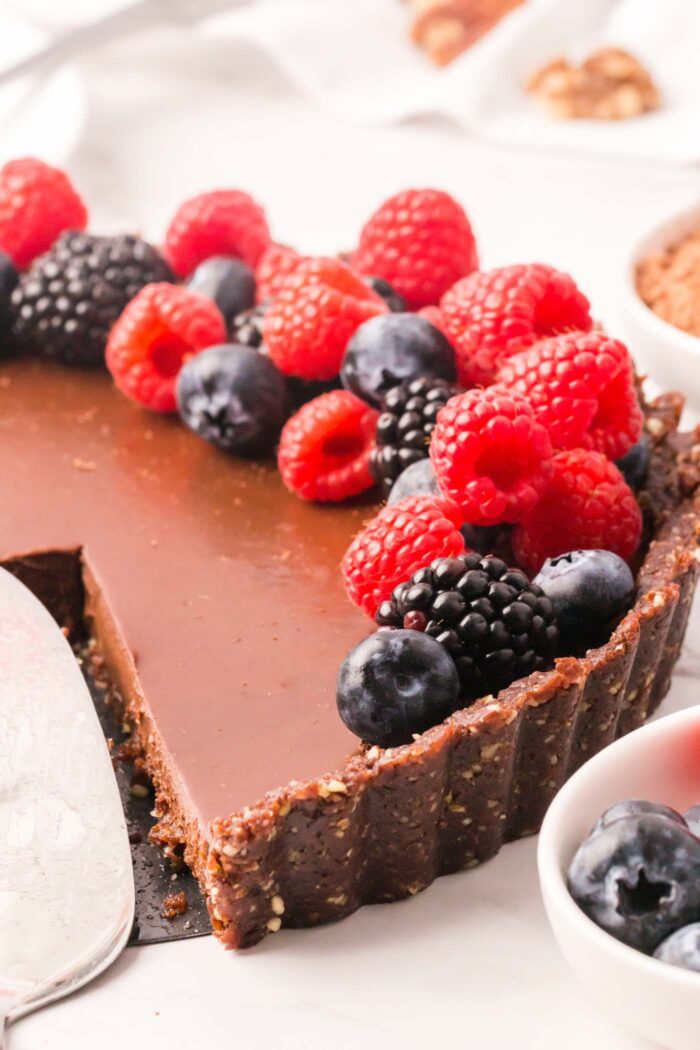 Close up of a chocolate tart with a chocolate crust topped with fresh raspberries, blueberries and blackberries.