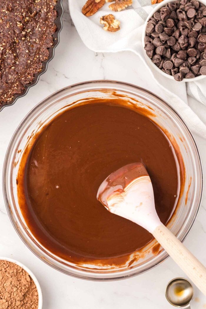 A creamy melted chocolate mixture in a mixing bowl with a spatula in it.