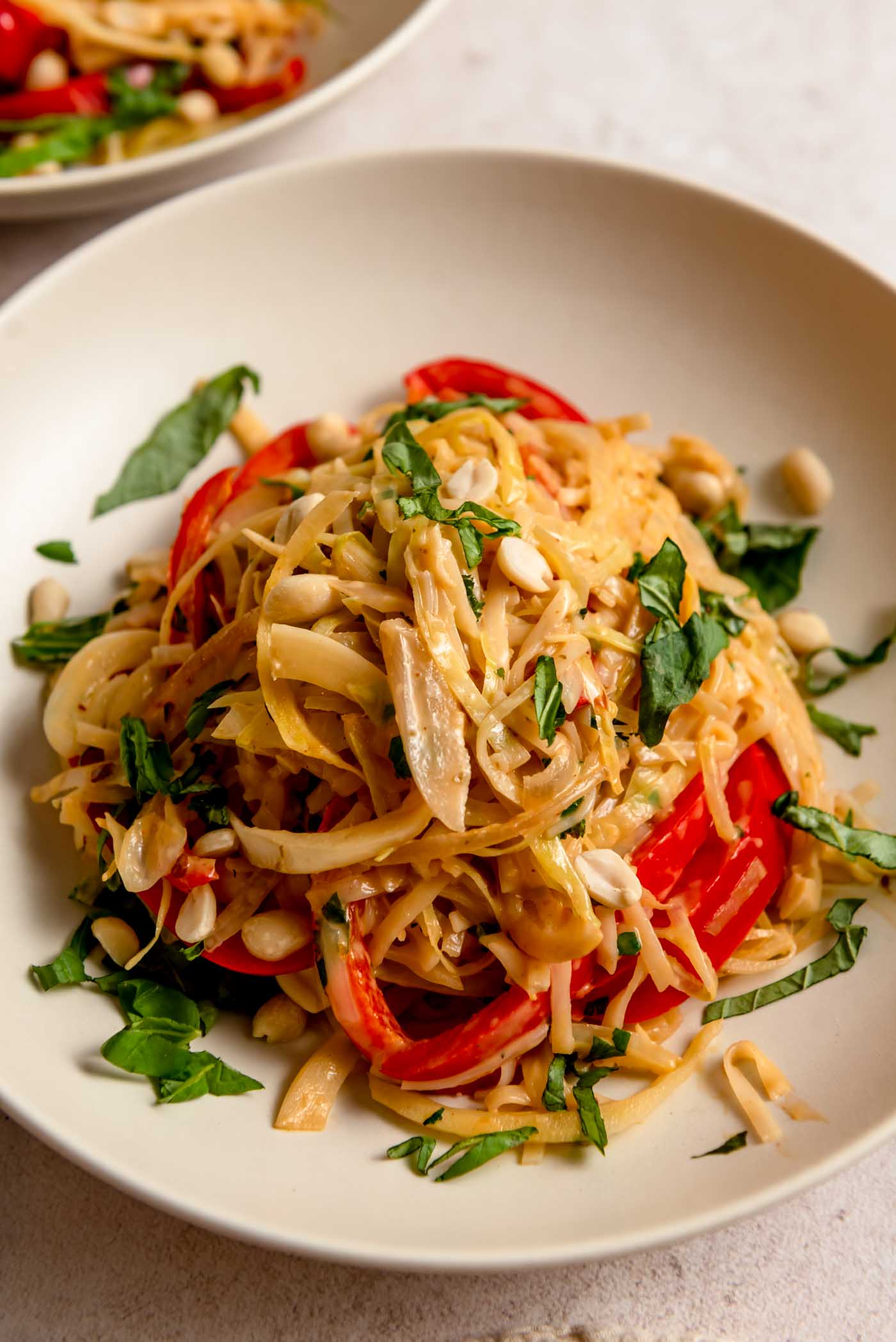 A bowl of Thai red curry noodles with bell pepper and cabbage, topped with basil and peanuts.