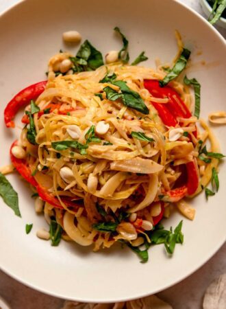Overhead view of a bowl of red curry noodles with sliced red bell peppers, cilantro, peanuts and onion.