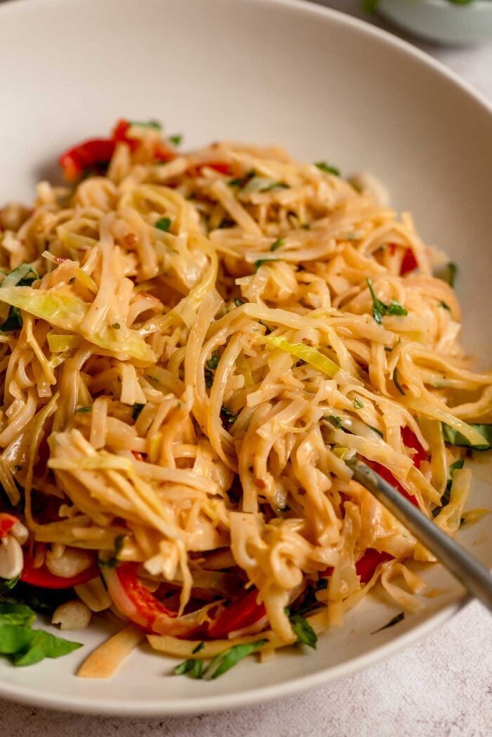 Creamy Thai red curry noodles with bell peppers and cabbage in a bowl with chopsticks.