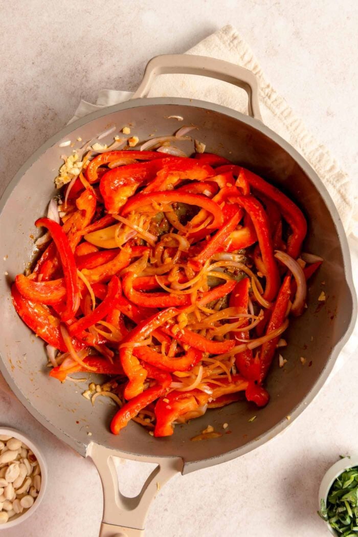 Sliced red bell peppers, red curry paste, shallot, onion and ginger in a non-stick pan.
