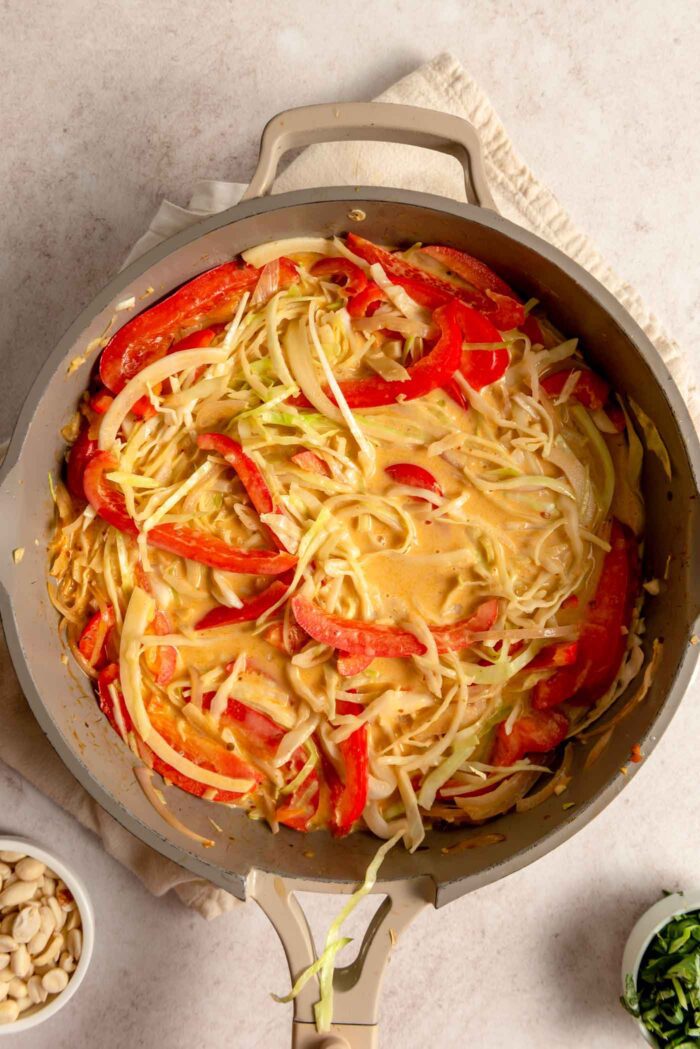 Cabbage and red bell pepper cooking in a red curry sauce in a pan..