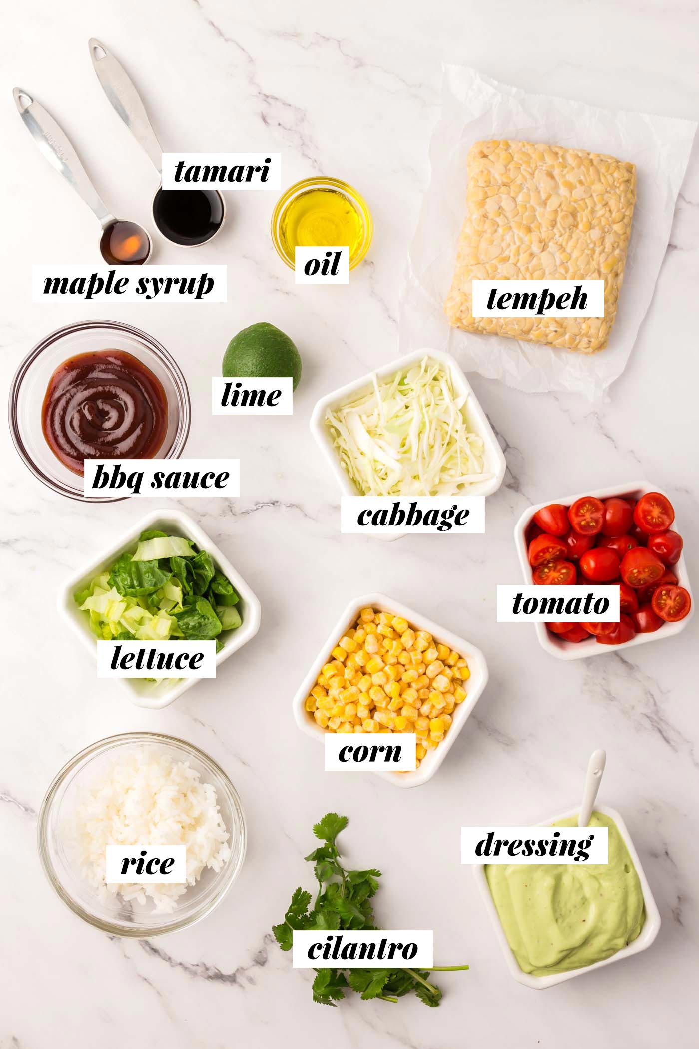 All the ingredients for a BBQ tempeh bowl with rice, tomatoes, corn and avocado dressing.  Each element is labeled with text.