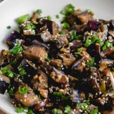 Close up of stir fried eggplant with green onion and sesame seeds in a bowl.