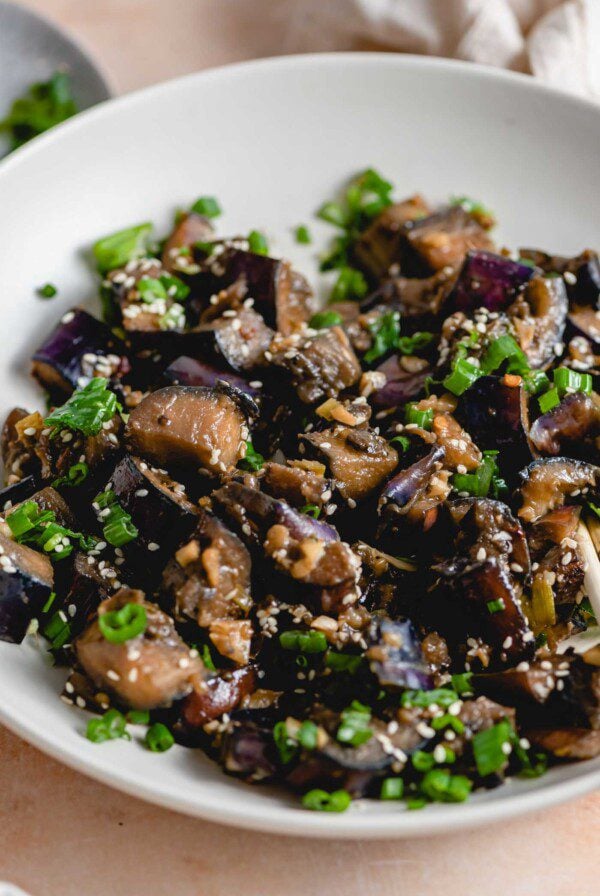 Close up of stir fried eggplant with green onion and sesame seeds in a bowl.