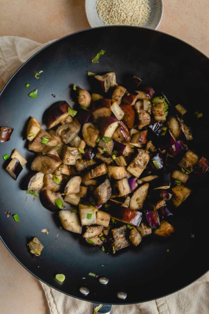 Stir fried cooked eggplant and green onion in a large wok.
