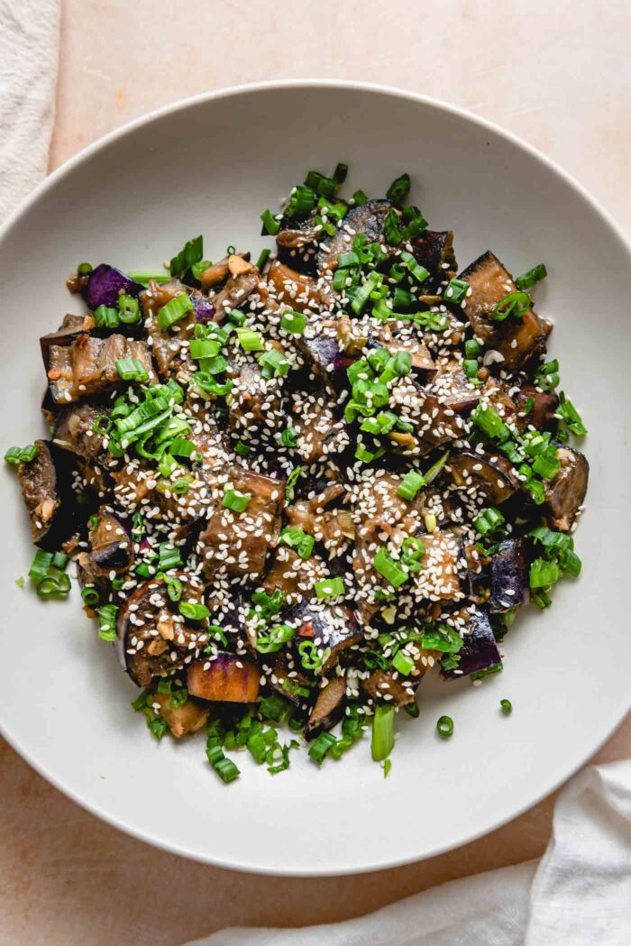 Stir fried eggplant topped with green onions and sesame seeds in a bowl.
