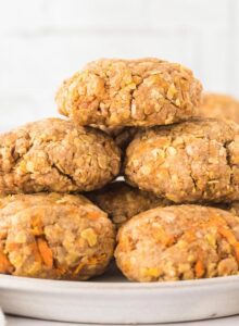 A plate of carrot cake oatmeal cookies in front of a white brick backsplash.