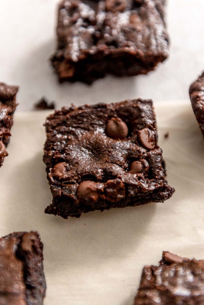 An avocado brownie with chocolate chips on a piece of parchment paper with more brownies around it.