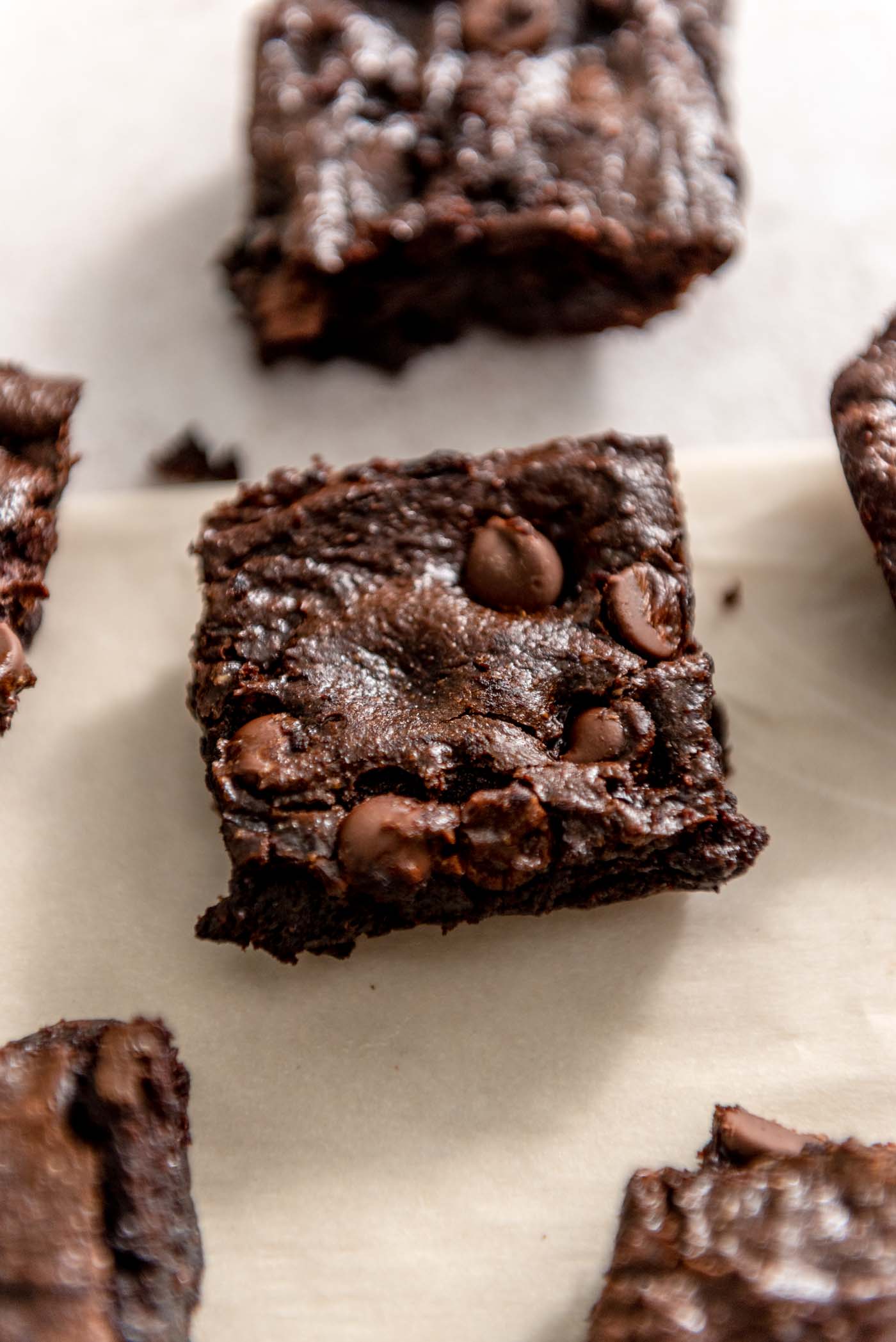 An avocado brownie with chocolate chips on a piece of parchment paper surrounded by more brownies.